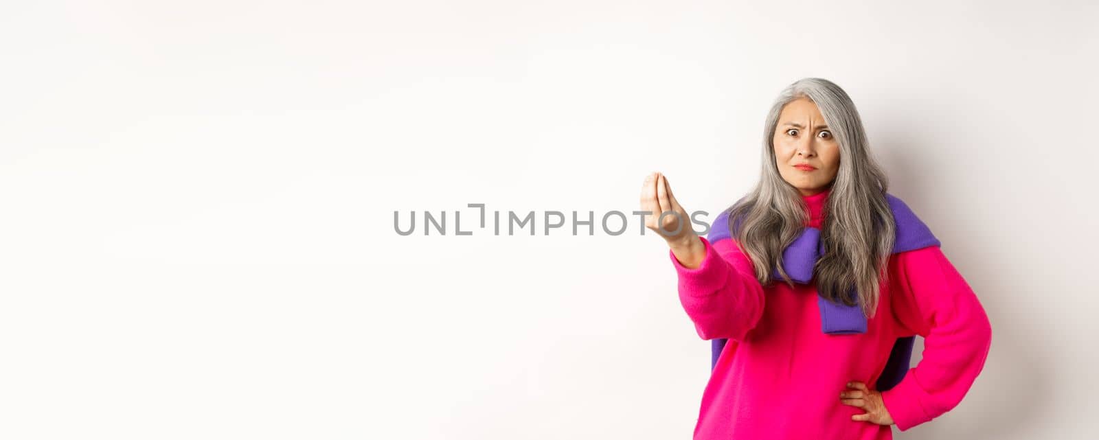 Funny asian woman staring angry and confused, shaking fingers, standing grumpy against white background. Copy space