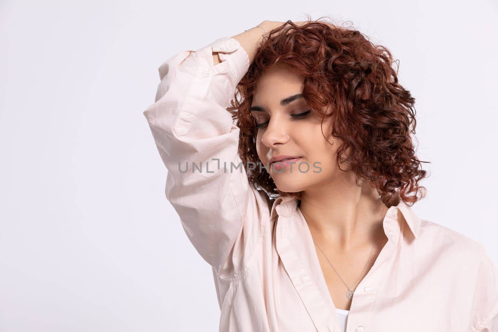 A hand on his head. Closed eyes. The pale complexion of a young European woman. A dreamy girl. Beautiful curly chestnut-colored hair. Natural hairstyle.