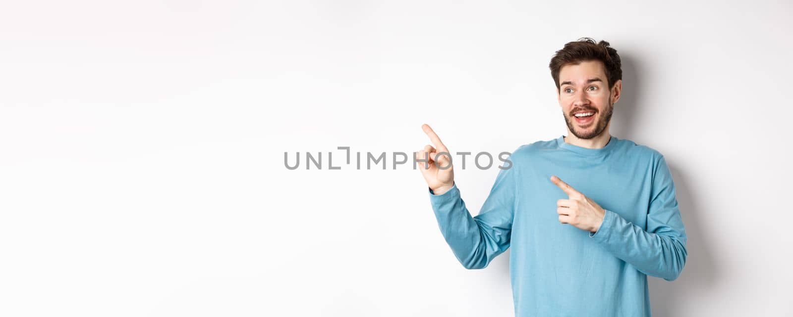 Excited bearded man checking out special offer, pointing and looking at advertisement with happy face, standing over white background.