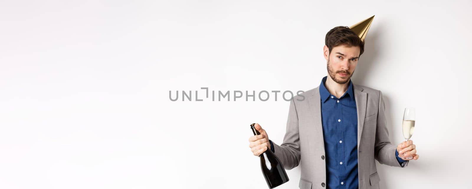 Party guy standing in birthday hat and celebrating, holding champagne bottle and glass, looking drunk, wearing grey suit by Benzoix