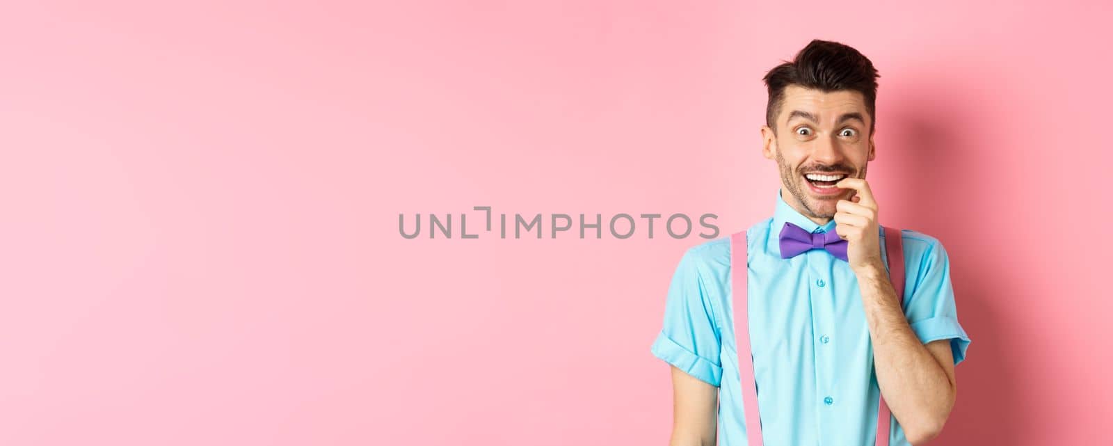 Excited and tempted young guy wants something, biting fingernail with temptation looking at camera, choosing product, standing over pink background by Benzoix