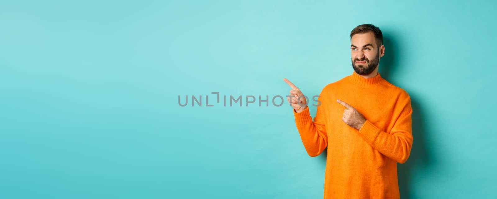 Displeased and skeptical guy grimacing, showing bad product, pointing fingers left with disappointment, standing turquoise background by Benzoix