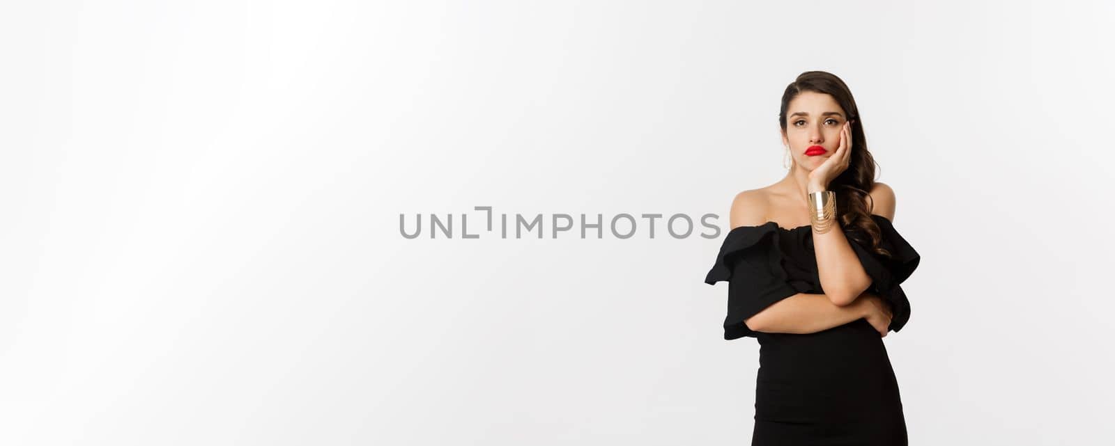 Fashion and beauty. Bored stylish woman in makeup, black dress, waiting for something, looking sad and gloomy, standing against white background by Benzoix