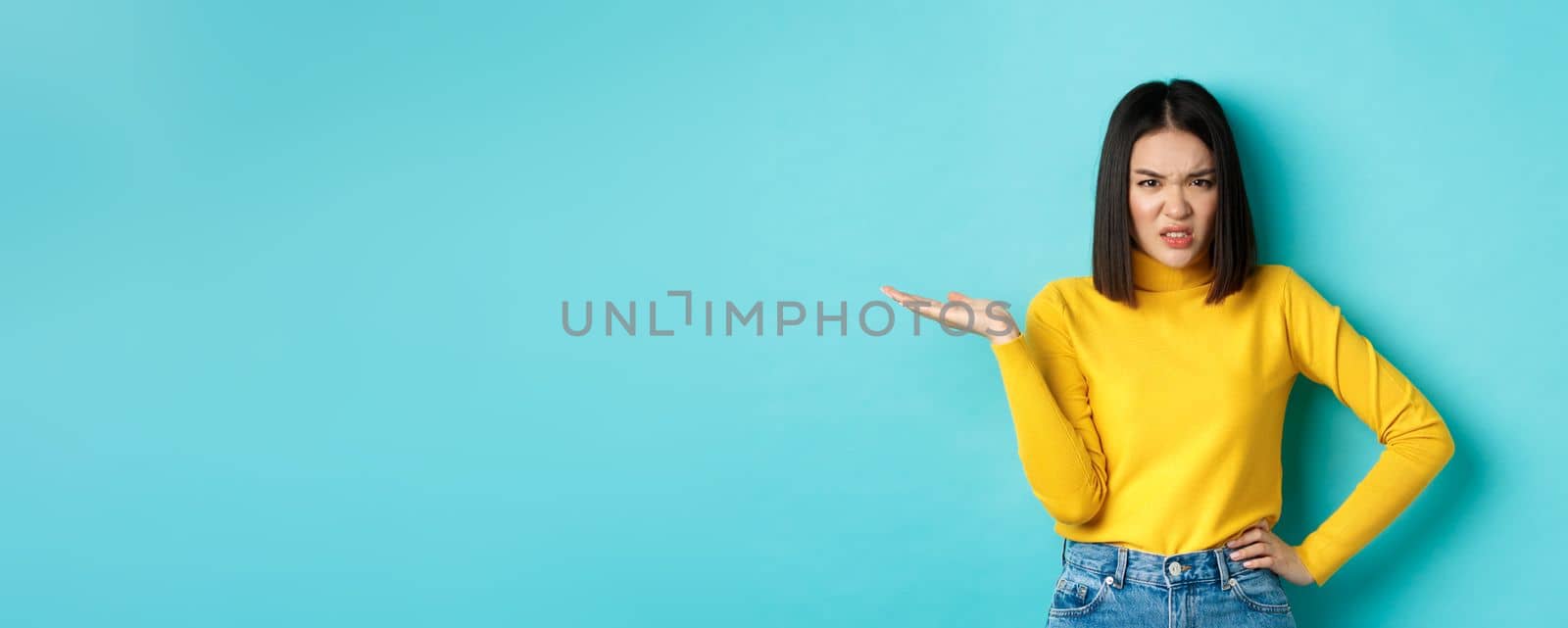 Frustrated and pissed-off asian girl raising hand up and grimacing bothered, staring at something with annoyance and disappointment, standing over blue background by Benzoix