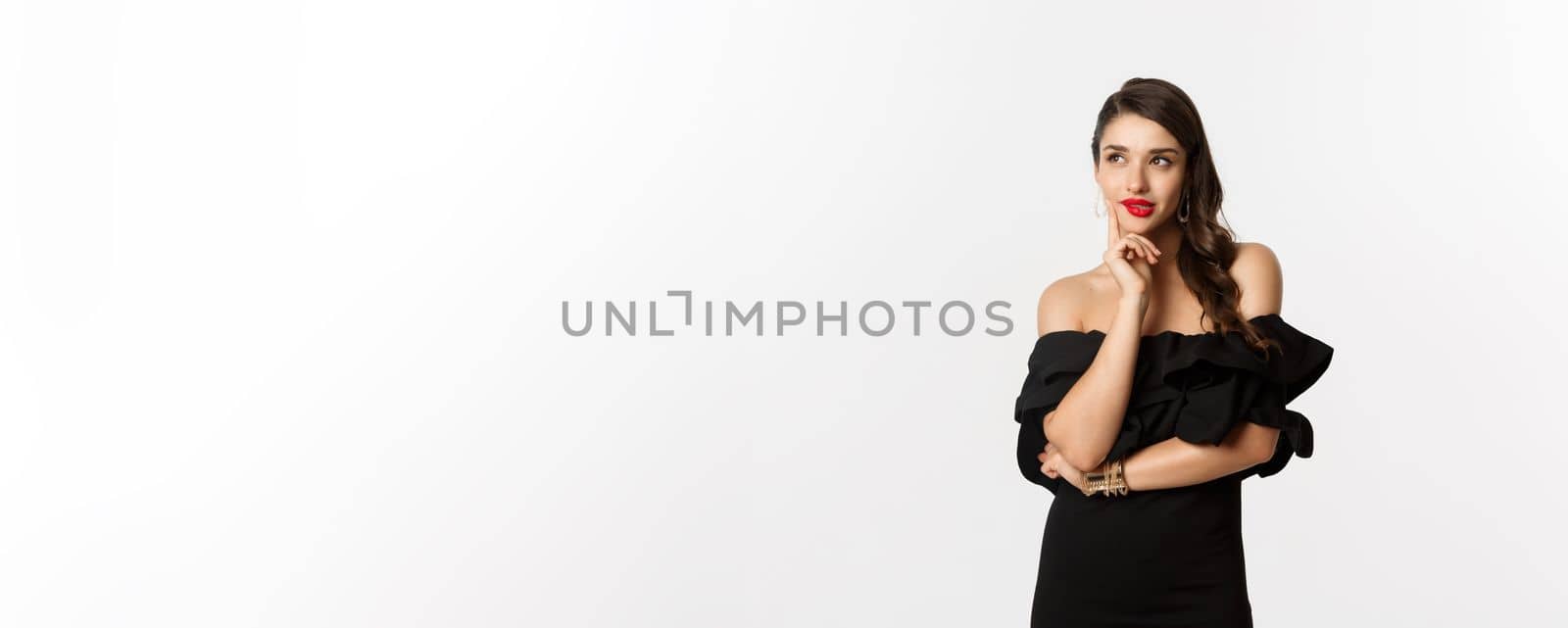 Fashion and beauty. Thoughtful young woman in black dress, smiling pleased and thinking, having an idea, white background.