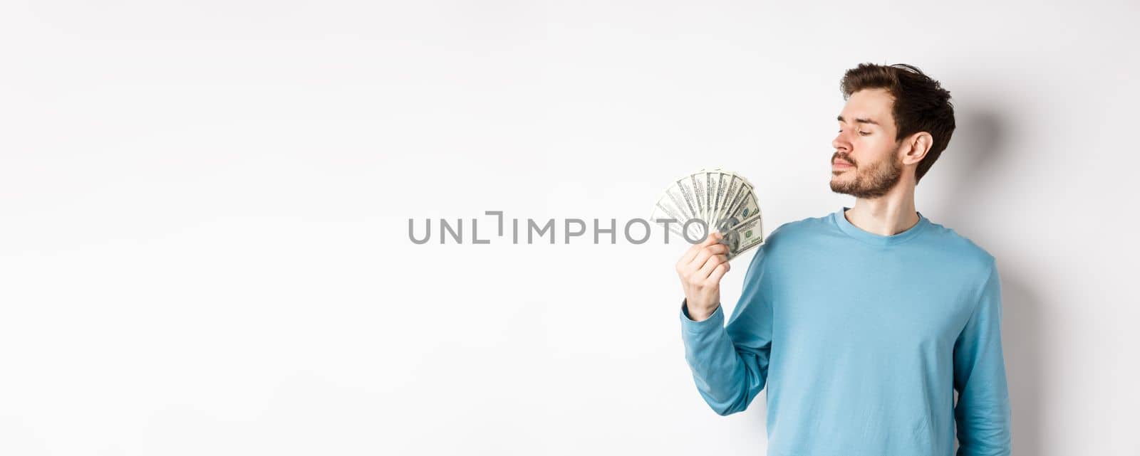 Handsome rich man with beard looking at money, got quick loan, standing over white background.