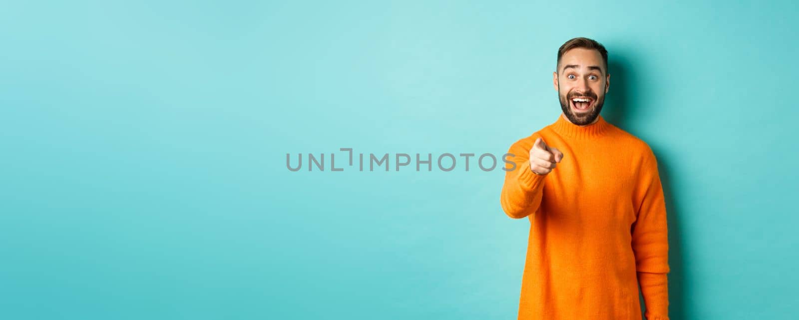 Surprised man stare happy and pointing at camera, recognize someone, excited about seeing something, standing over light blue background by Benzoix