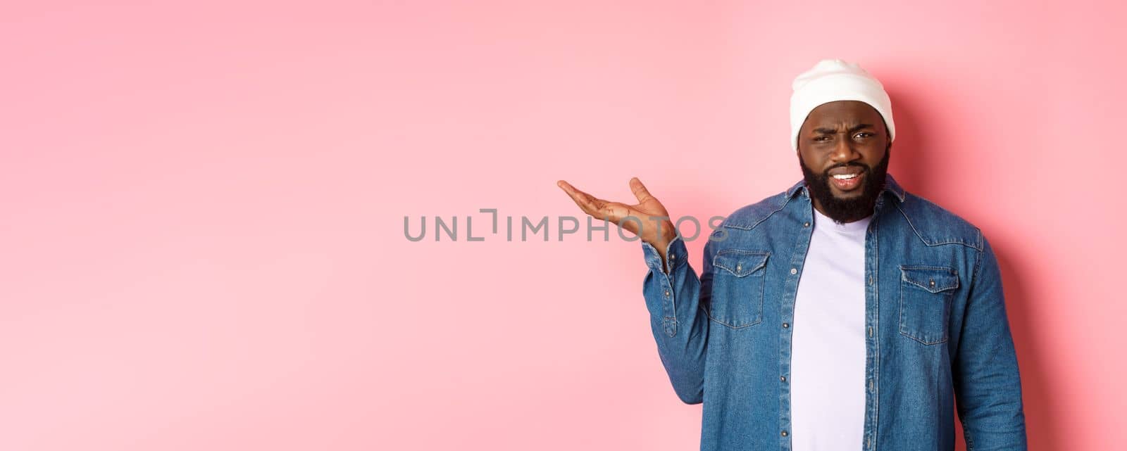 Annoyed and confused Black man arguing, raising hand up and staring at camera puzzled, cant understand wtf, standing over pink background.