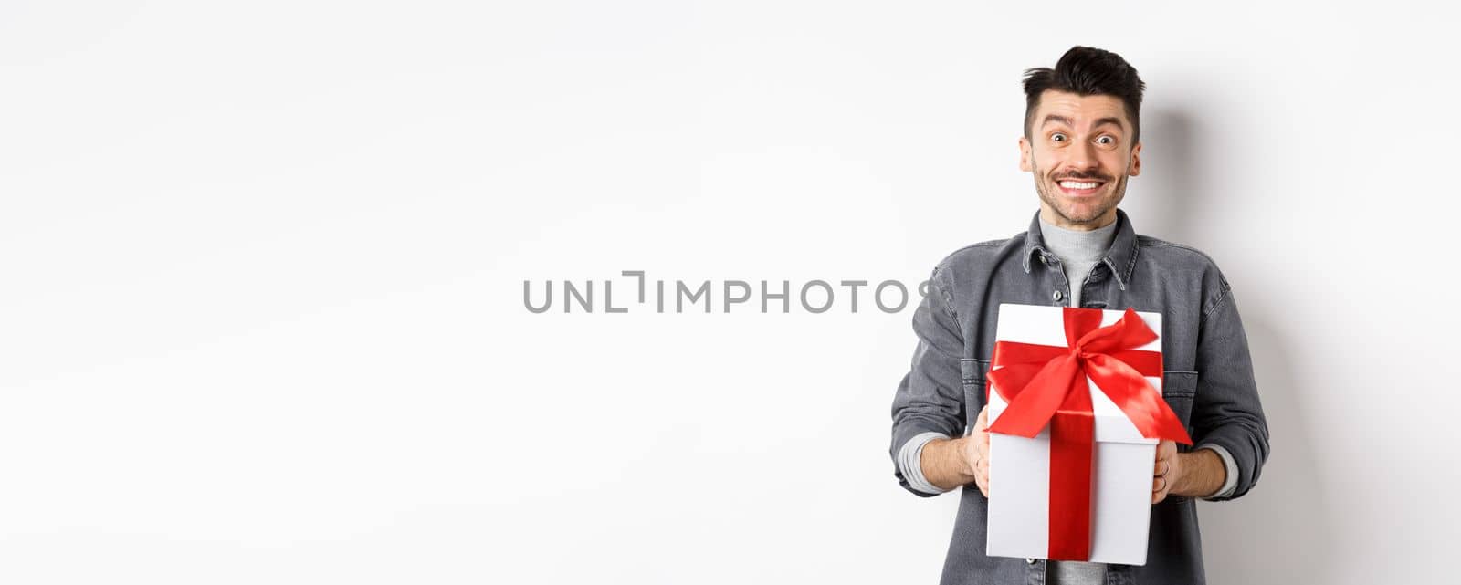 Cheerful caucasian guy holding surprise gift, receive present on holiday and smiling thankful, looking grateful at camera, celebrating Valentines day, white background.