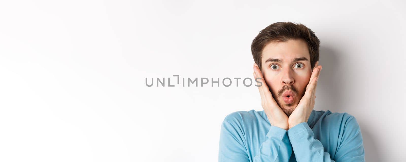 Close-up of impressed man checking out special offer, saying wow and touching face with amazed expression, stare at camera in awe, standing over white background by Benzoix