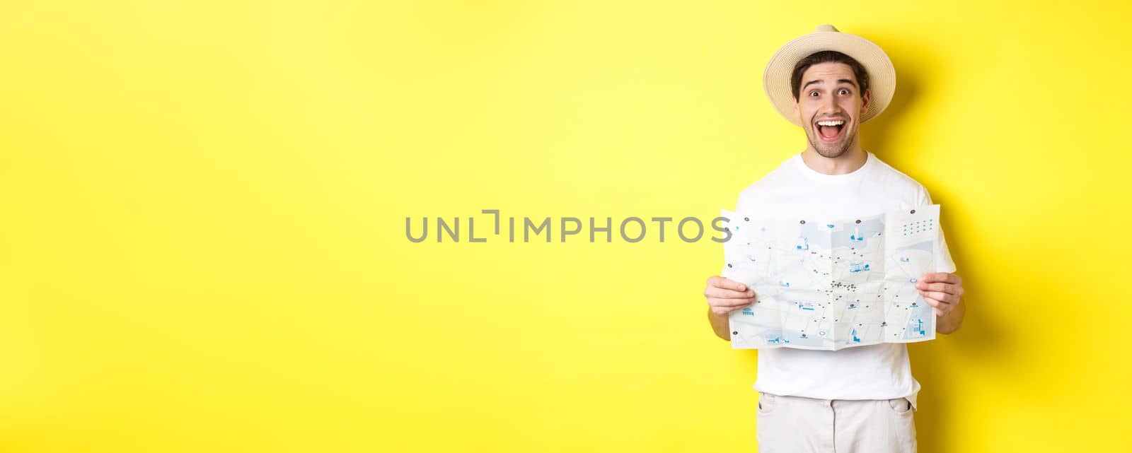 Travelling, vacation and tourism concept. Excited man tourist going sightseeing with map, standing over yellow background by Benzoix