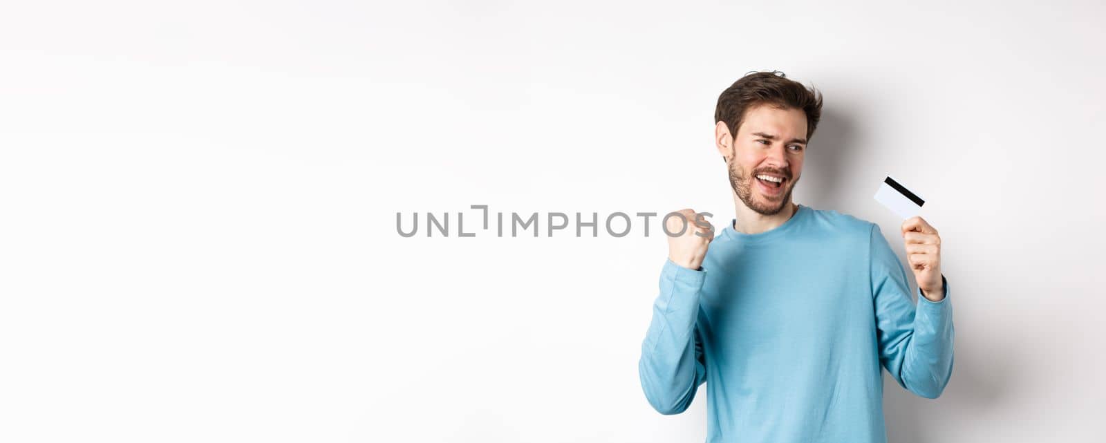 Happy man dancing with plastic credit card, smiling and saying yes, celebrating on white background. Copy space