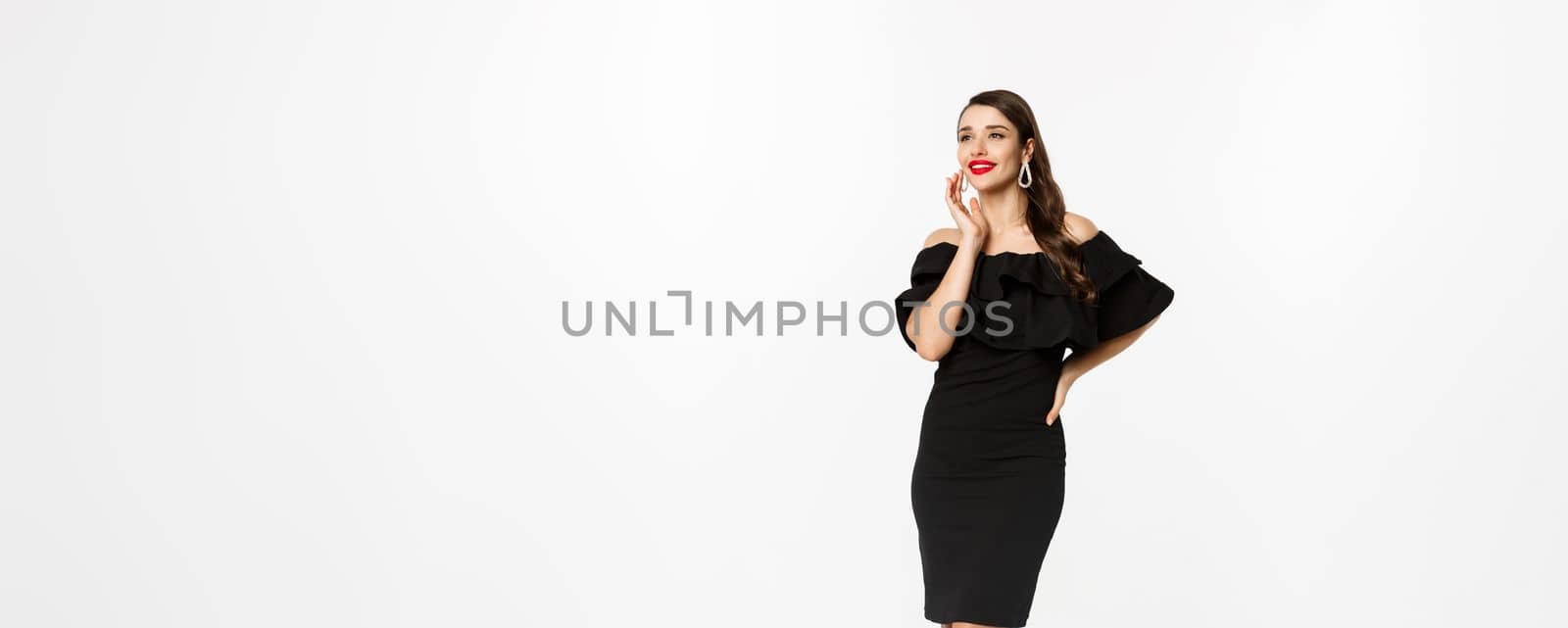 Vertical shot of attractive woman standing in elegant black dress with christmas gifts, smiling happy, standing over white background.