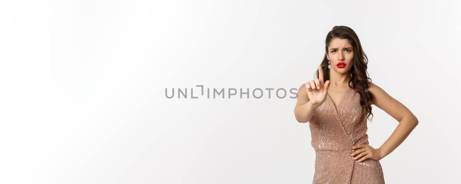 Concept of celebration, holidays and party. Displeased serious woman in glamour dress shaking fingers disapproval, prohibit something, telling no, white background.