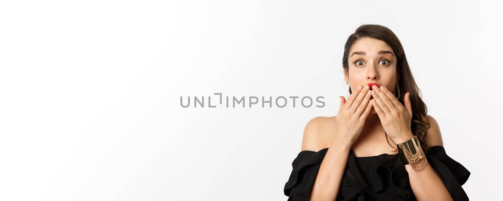 Fashion and beauty concept. Close-up of excited young woman looking amazed, cover mouth with hands and staring at camera with rejoice, white background.