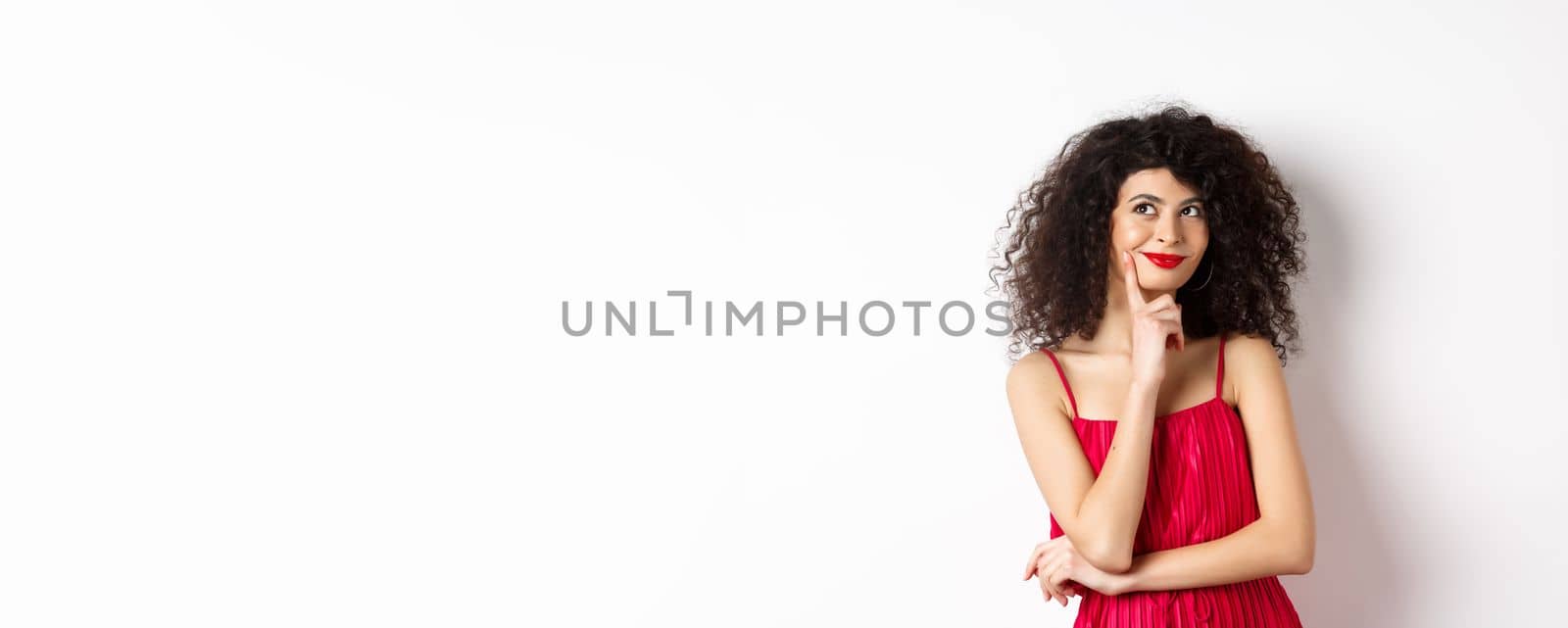 Image of elegant woman in red dress, looking pensive and smiling, thinking of romantic date, standing over white background by Benzoix