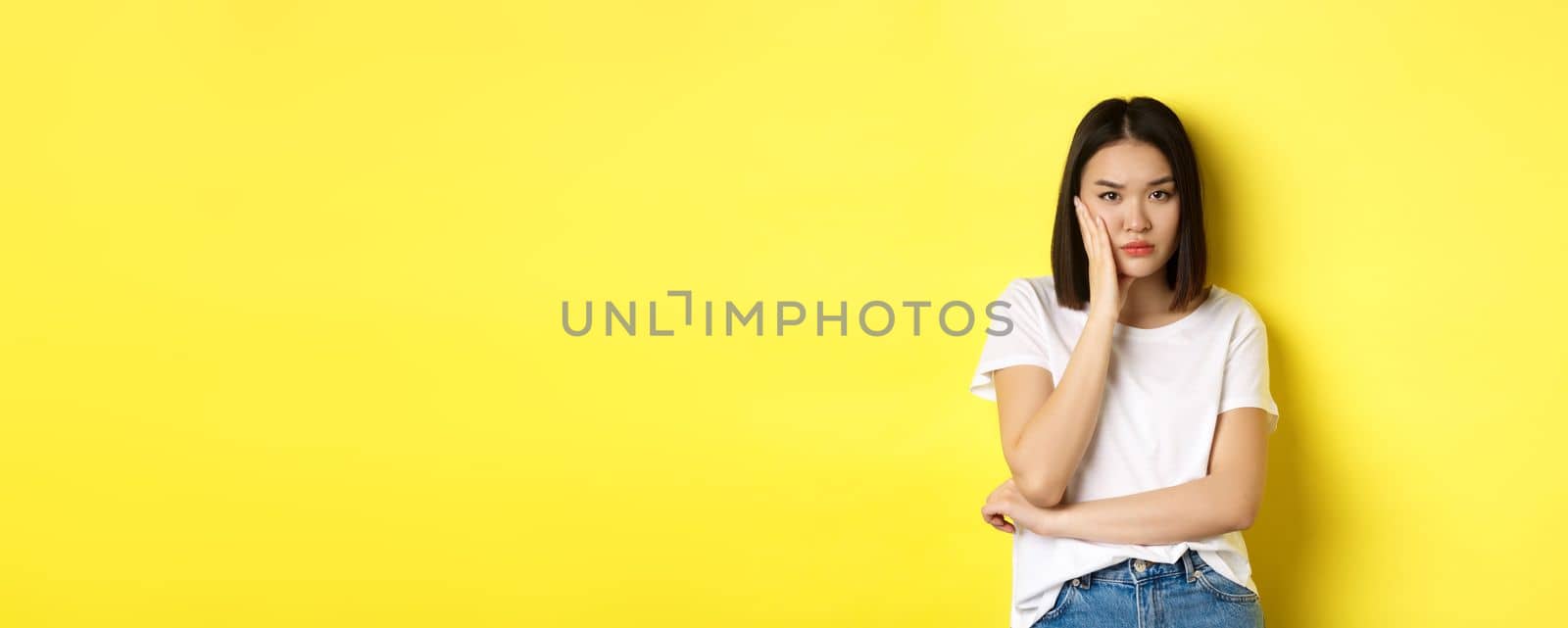 Bored and annoyed asian woman tired of listening, looking skeptical at camera, standing over yellow background by Benzoix