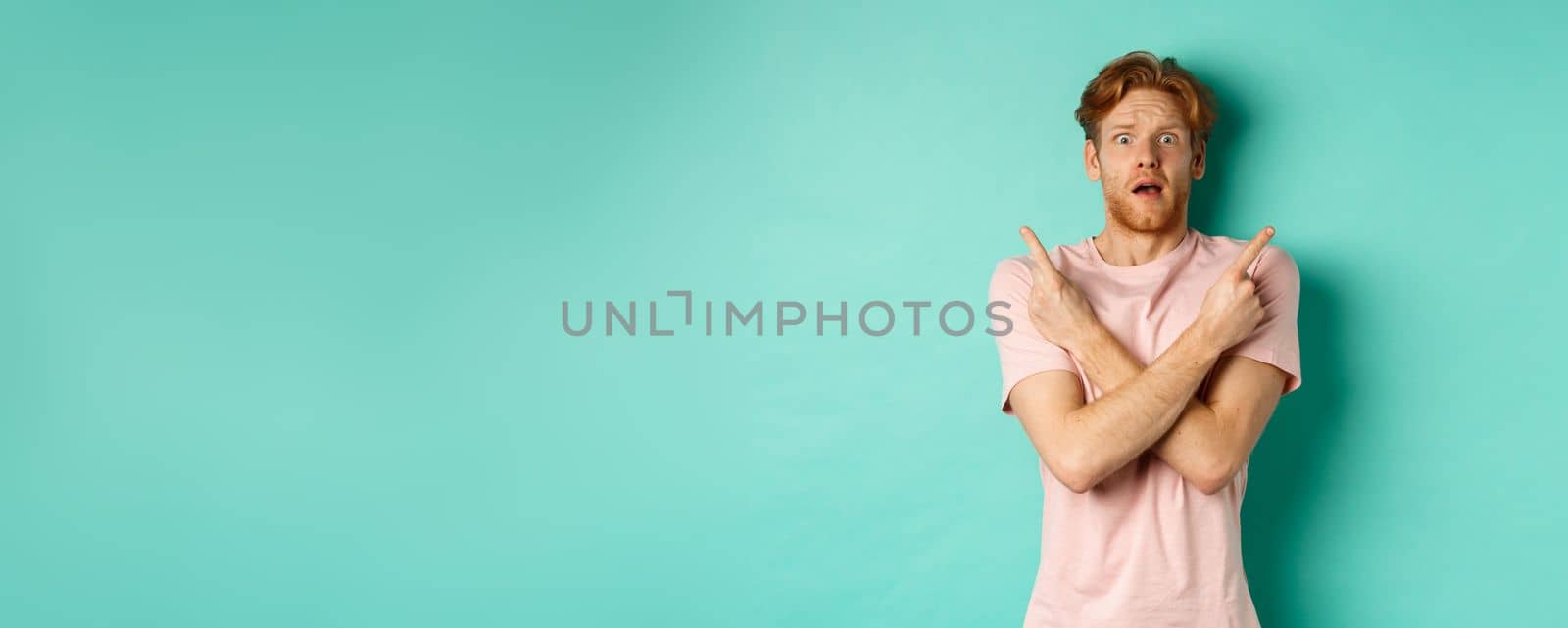 Nervous guy with red hair staring indecisive, cross arms and pointing sideways, showing two variants with puzzled face, standing in t-shirt over mint background.