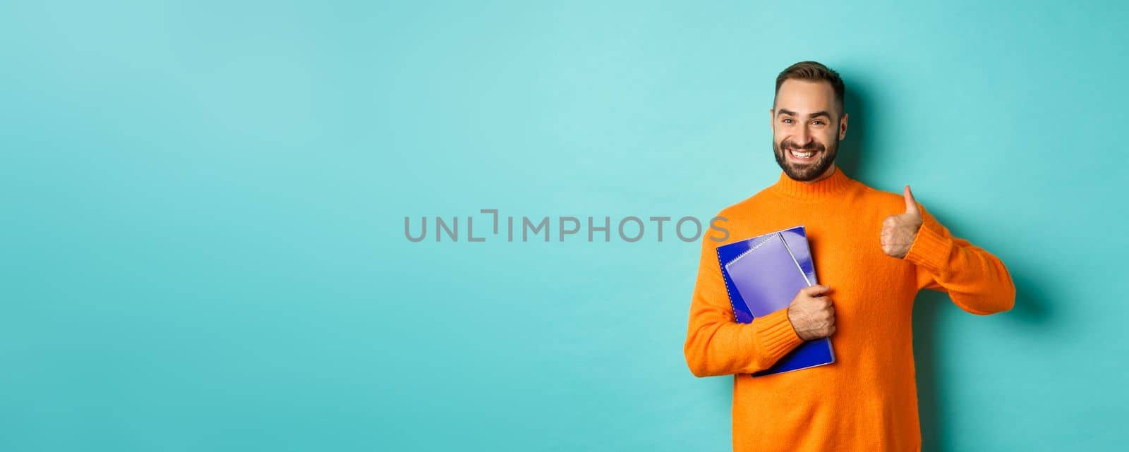 Education. Smiling bearded man holding notebooks and smiling, going on courses, showing thumbs-up in approval, like something, standing over turquoise background.