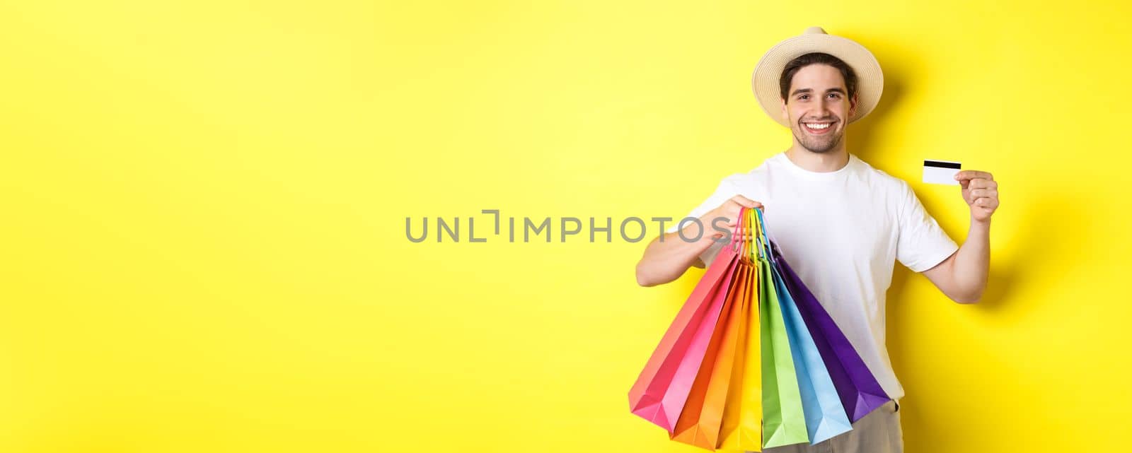 Happy attractive guy showing shopping bags and credit card, concept of banking and easy payment, standing over yellow background by Benzoix