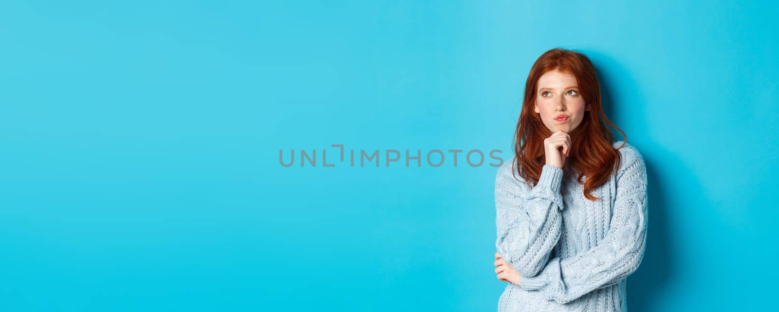 Pretty teenage girl with red hair thinking, looking upper left corner thoughtful, pondering something, standing over blue background by Benzoix