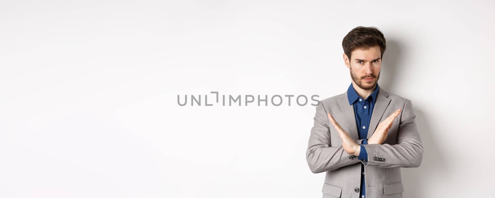 Serious business man making cross and says no, looking determined, disagree and prohibit something bad, tell to stop, standing in suit on white background.