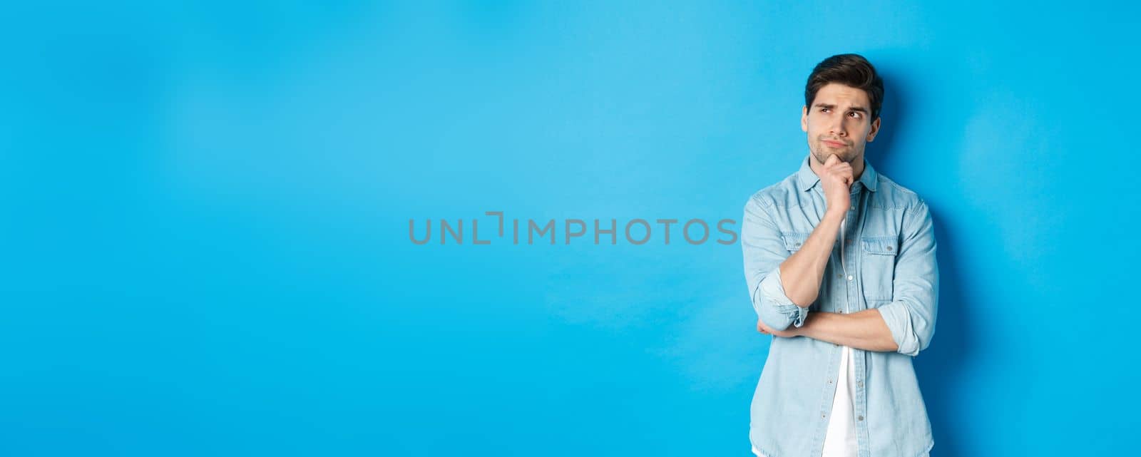 Image of adult bearded man 25s years, thinking about something, looking at upper left corner and pondering ideas, standing over blue background by Benzoix