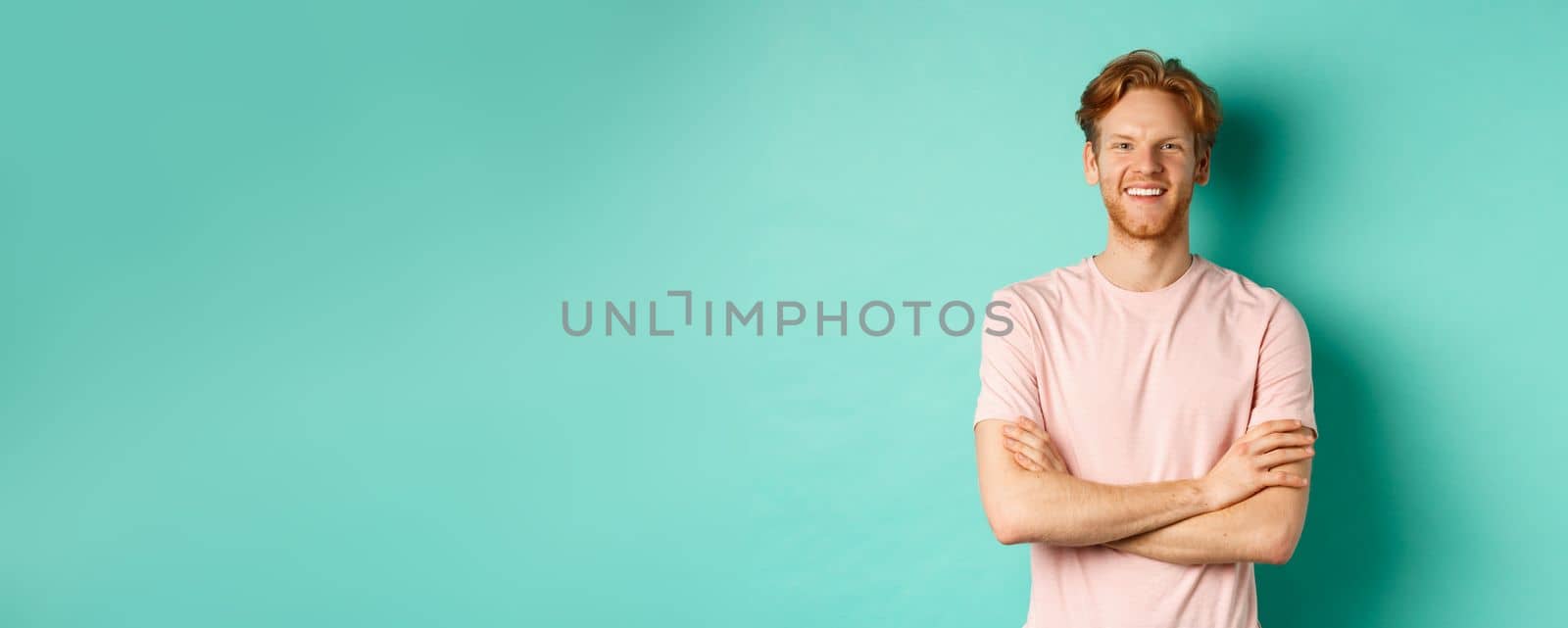 Portrait of friendly-looking young man with red hair and beard smiling and starng satisfied, holding hands crossed on chest, standing over turquoise background by Benzoix
