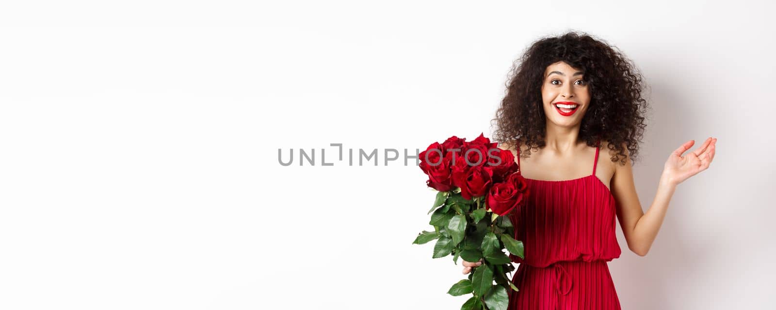 Romance and Valentines day. Woman gasping surprised and happy, receive surprise gift from lover, holding bouquet of red roses, standing on white background.