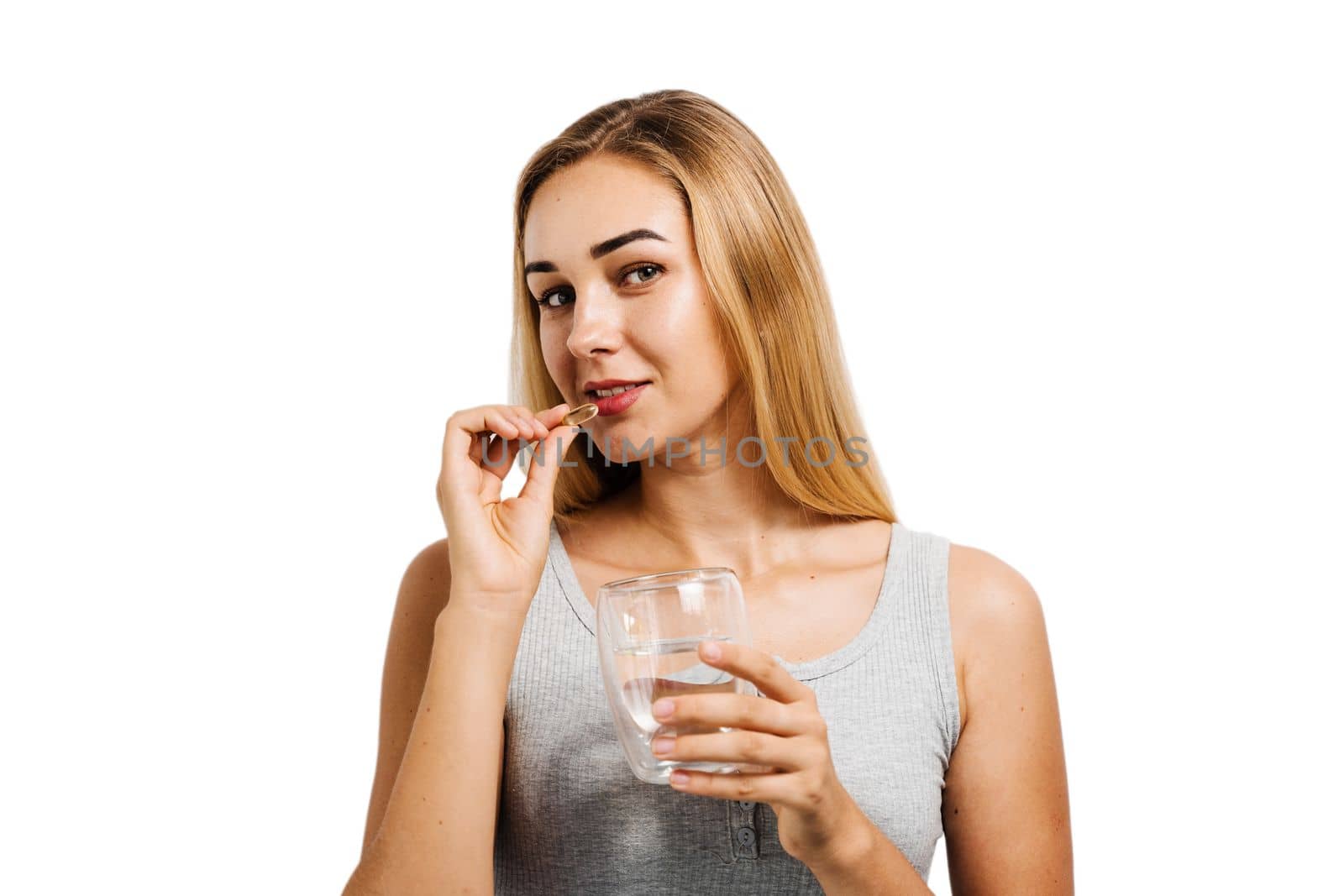 Girl with Omega-3 capsule and cup of water is taking a BADS capsule on white background. Biologically active dietary supplements. Taking vitamin D for building and maintaining healthy bones