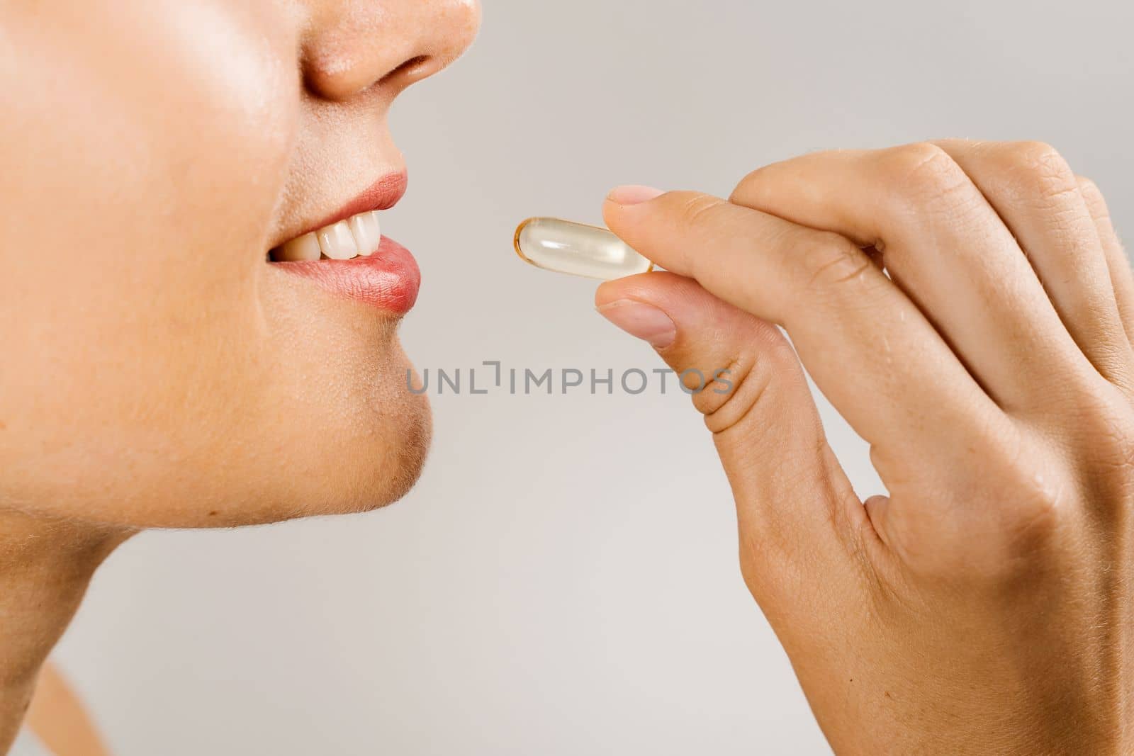 Omega 3 pill of fish fat oil near lips close-up. BADS capsule of biologically active dietary supplements. Vitamin D for building and maintaining healthy bones