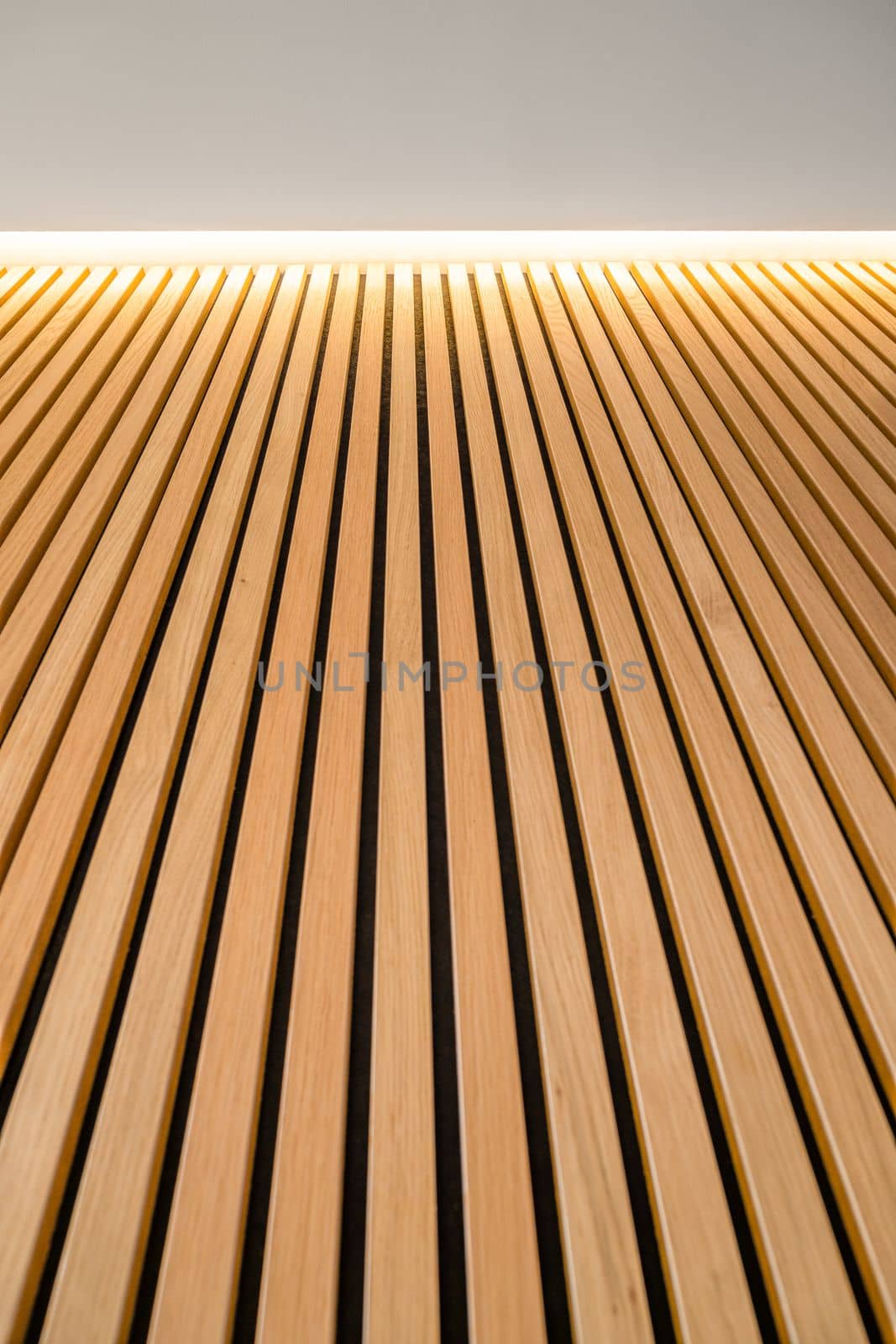 Covering with vertical wooden smooth planks is illuminated from above by artificial light. Light wood panels with a beautiful texture. Part of the interior of the room with an individual design