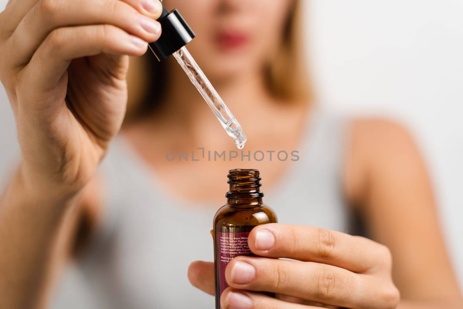 Face serum pipette close-up in hands of attractive girl on white background. Girl applies face serum to her face with pipette on white background. by Rabizo
