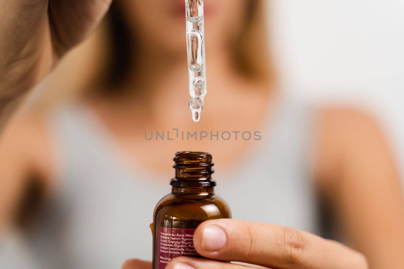 Face serum pipette close-up in hands of attractive girl on white background. Girl applies face serum to her face with pipette on white background