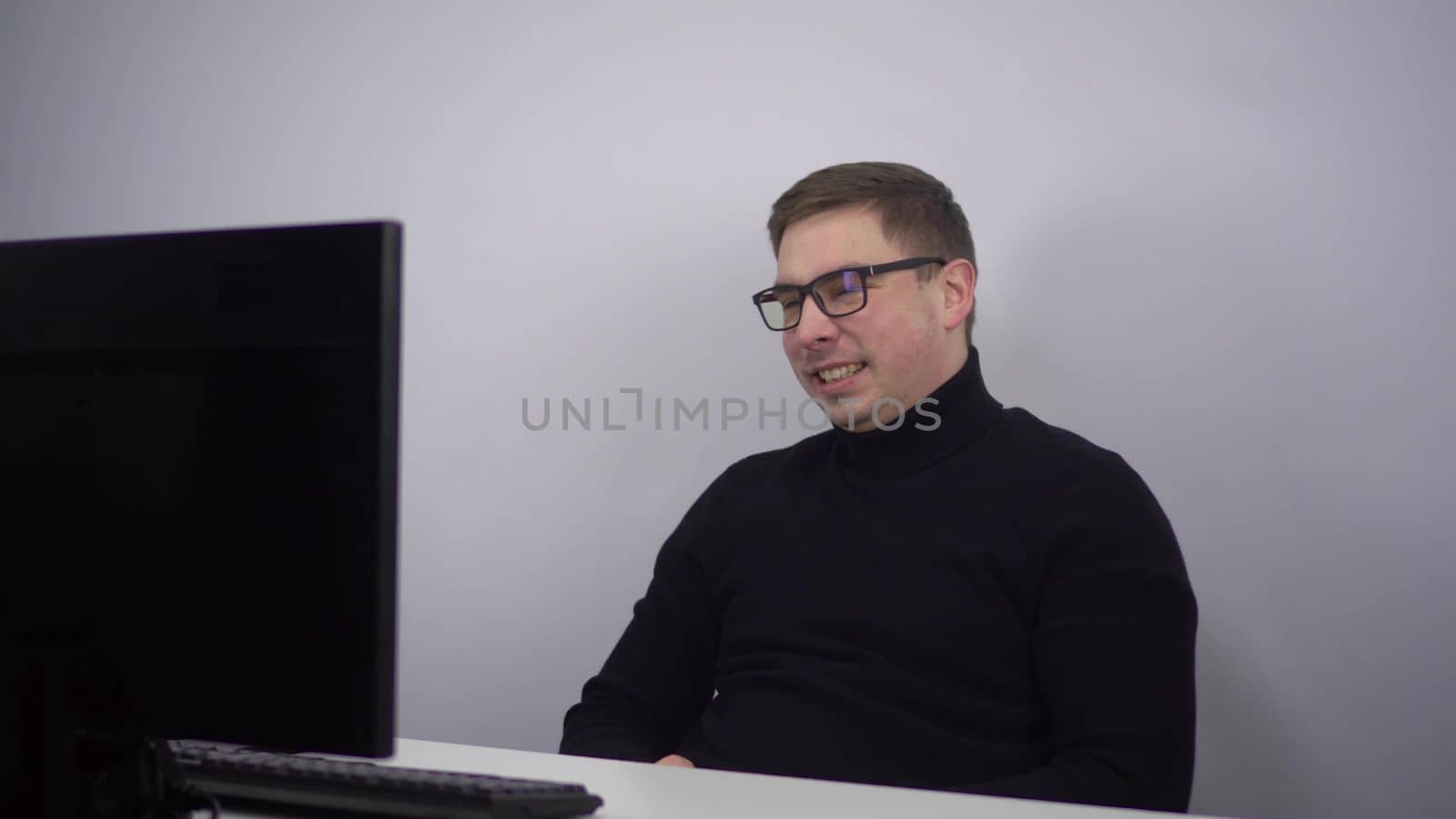 A young man looks at a computer monitor and laughs emotionally. An IT specialist in glasses sits in the office and watches a movie. 4k