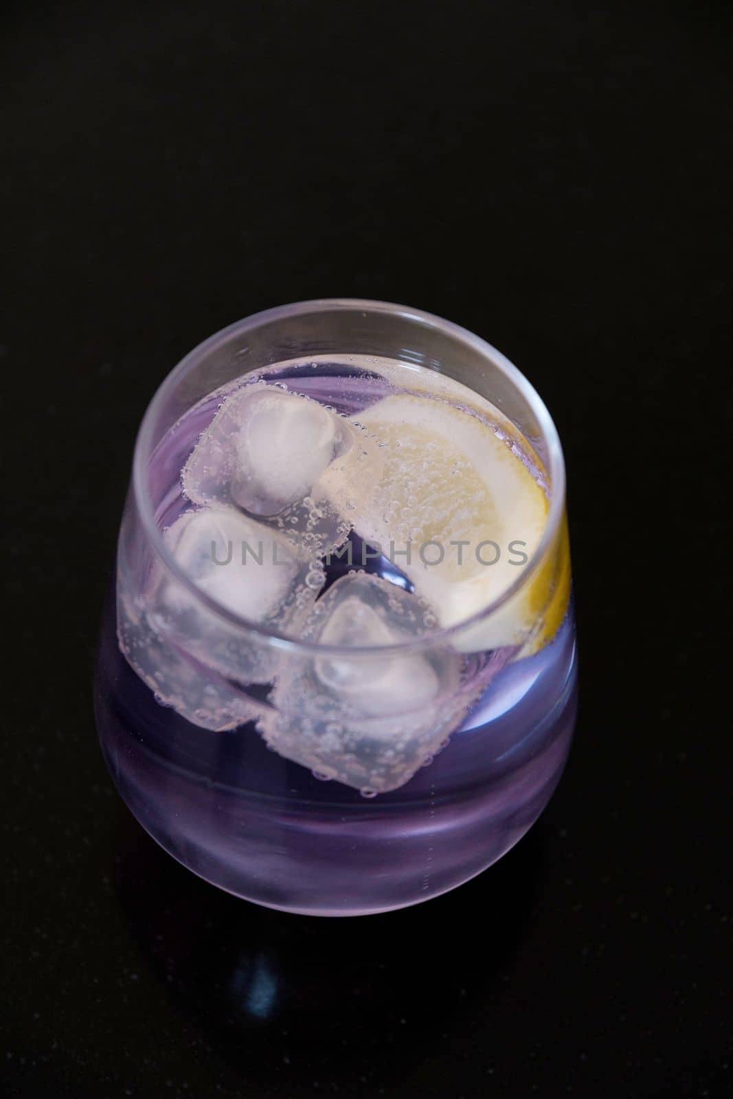 refreshing drink gin and tonic of purple color in a transparent glass on a black background. High quality photo