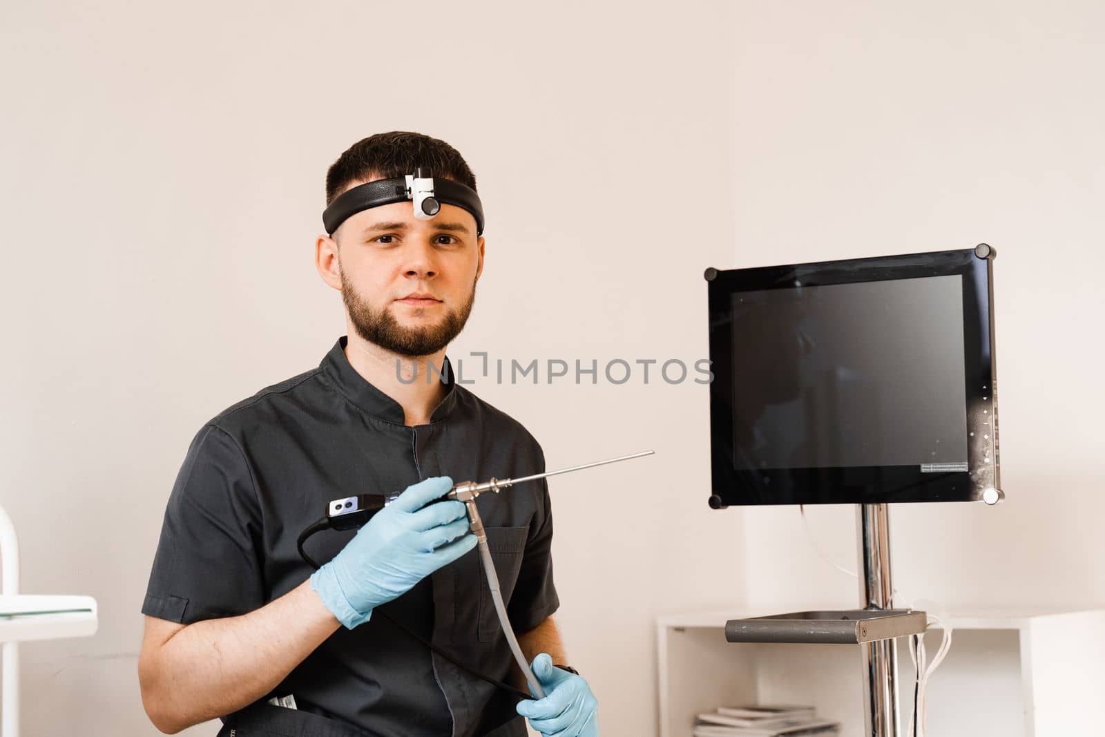 ENT doctor otolaryngologist with endoscope in hands. Prepearing for endoscopy procedure. Doctor with headlight. by Rabizo