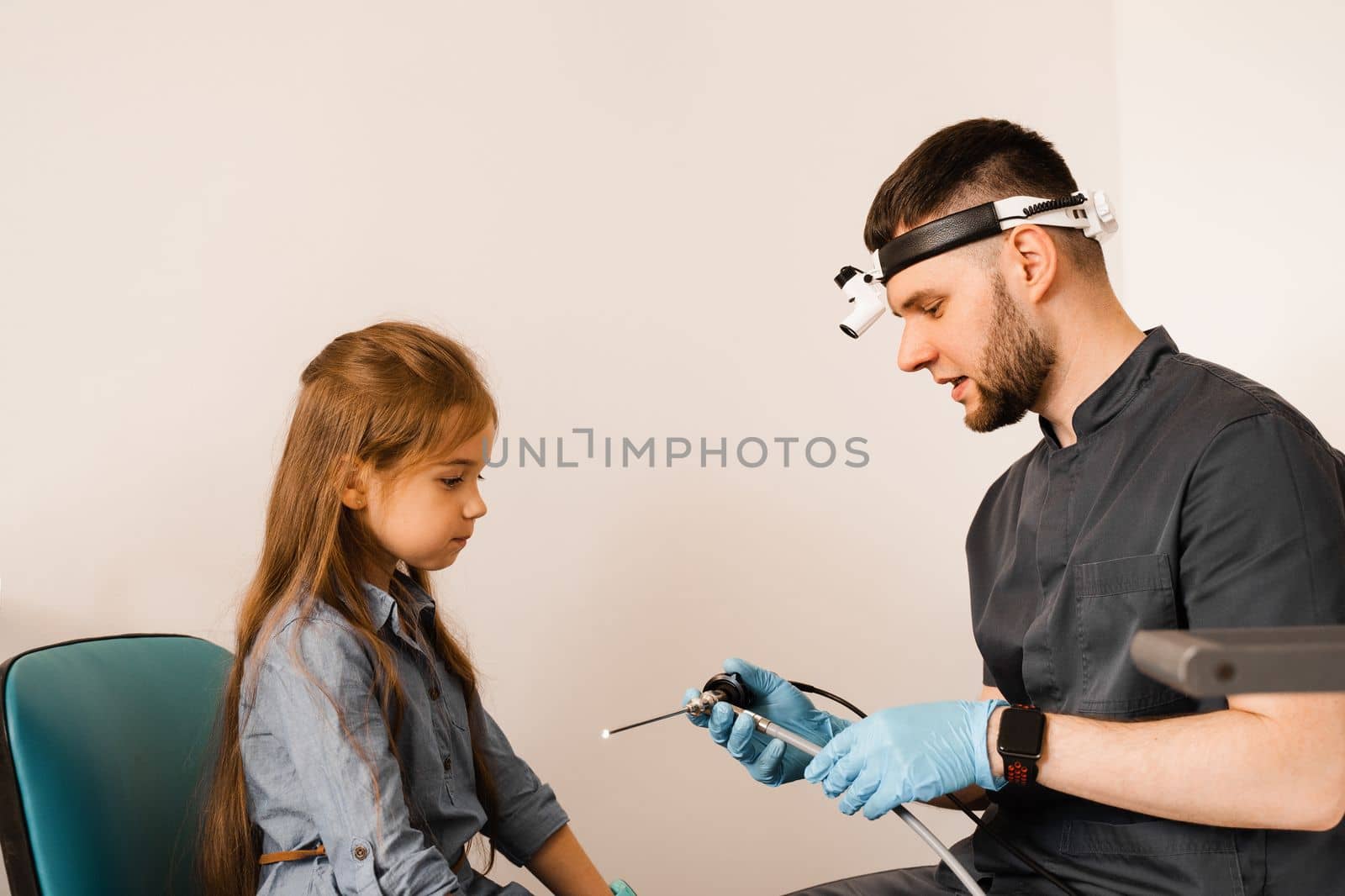 ENT doctor otolaryngologist with headlight showing to child endoscope for rhinoscopy and otoscopy. Nose and ears endoscopy of child