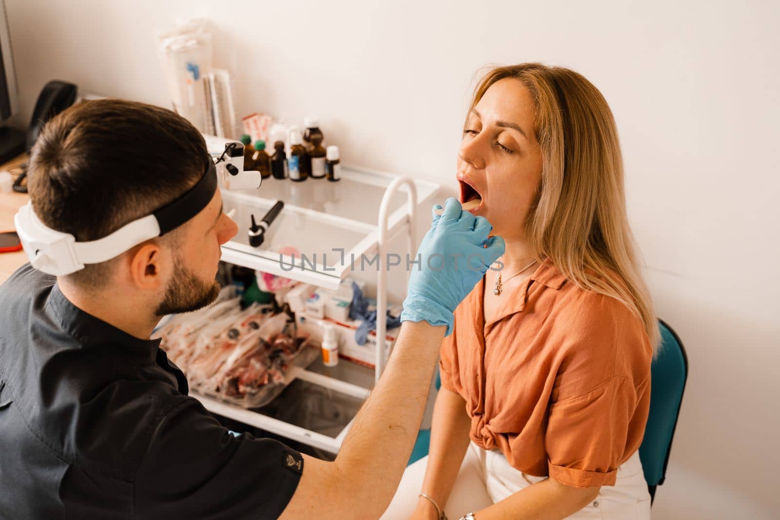 Oropharyngoscopy procedure. Otolaryngologist examines woman throat with spatula. Consultation with laryngologist. by Rabizo