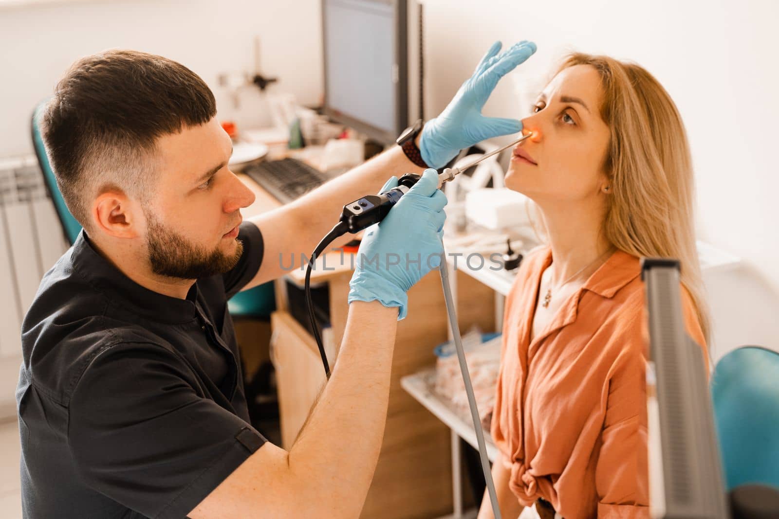 Nose endoscopy. Rhinoscopy procedure with rhinoscope. ENT doctor otolaryngologist with headlight treat nose woman patient. by Rabizo