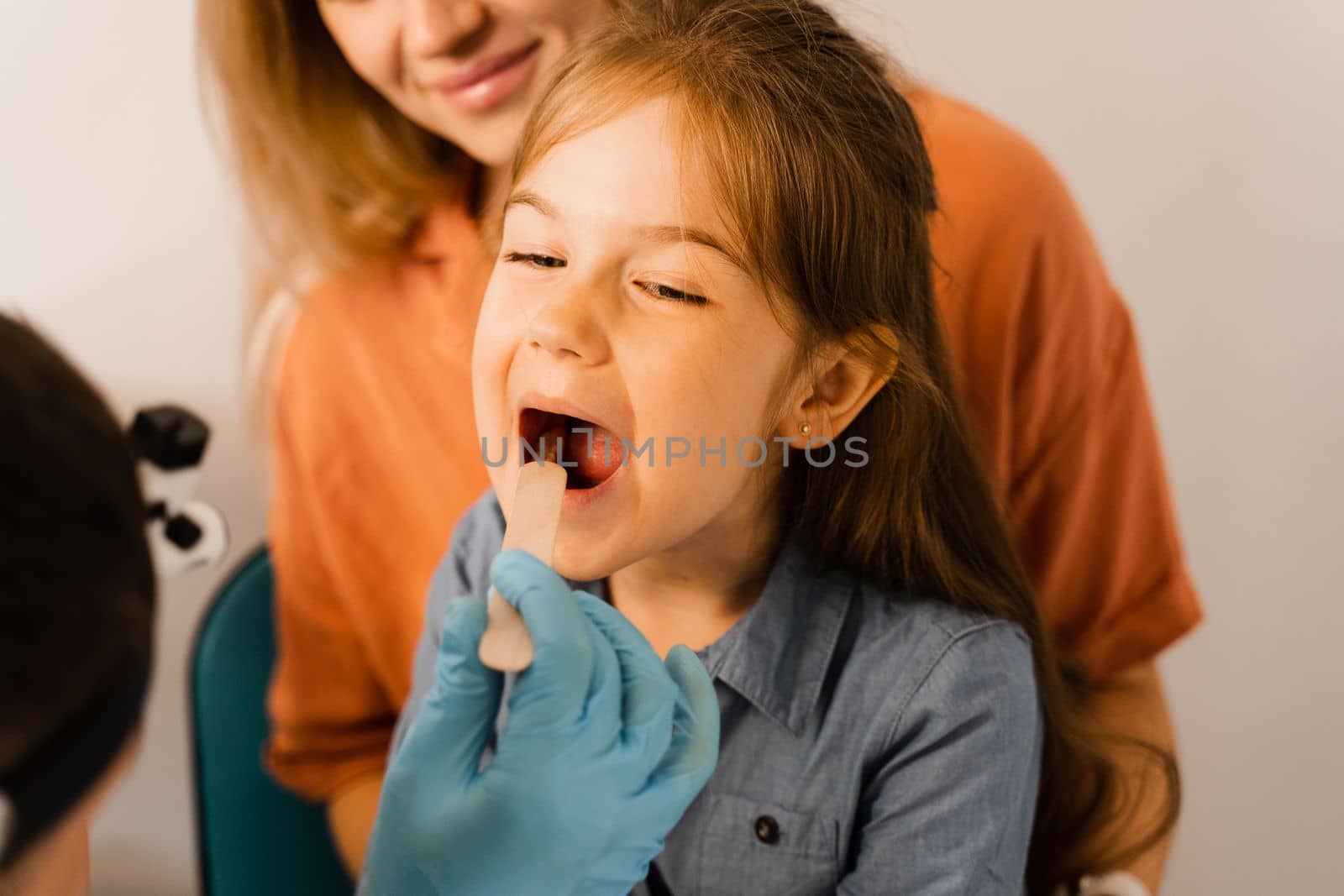 Oropharyngoscopy procedure for child. Otolaryngologist examines child throat with spatula. Family consultation with laryngologist