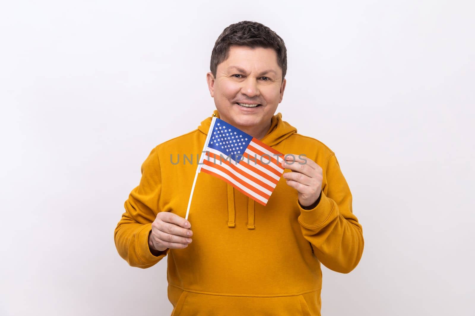 Portrait of smiling middle aged man holding USA national flag, celebrating national Independence Day - 4th july, wearing urban style hoodie. Indoor studio shot isolated on white background.