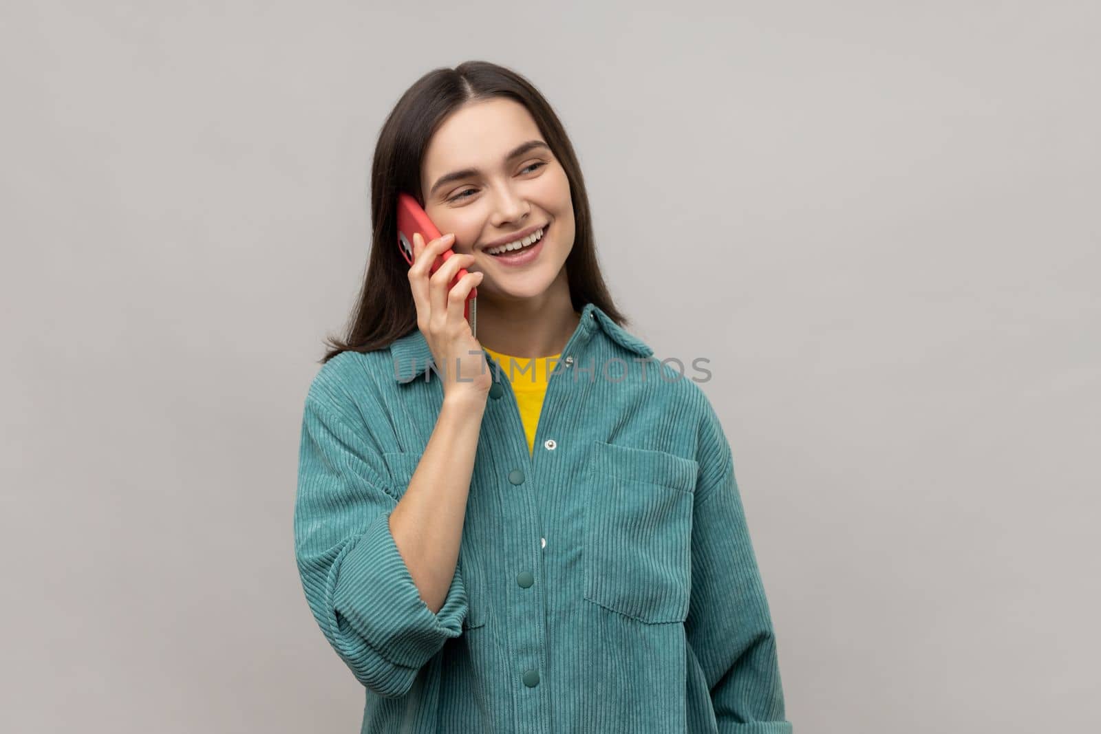 Beautiful young adult woman talking phone and smiling, pleasant conversation with boyfriend, making appointment or date, wearing casual style jacket. Indoor studio shot isolated on gray background.