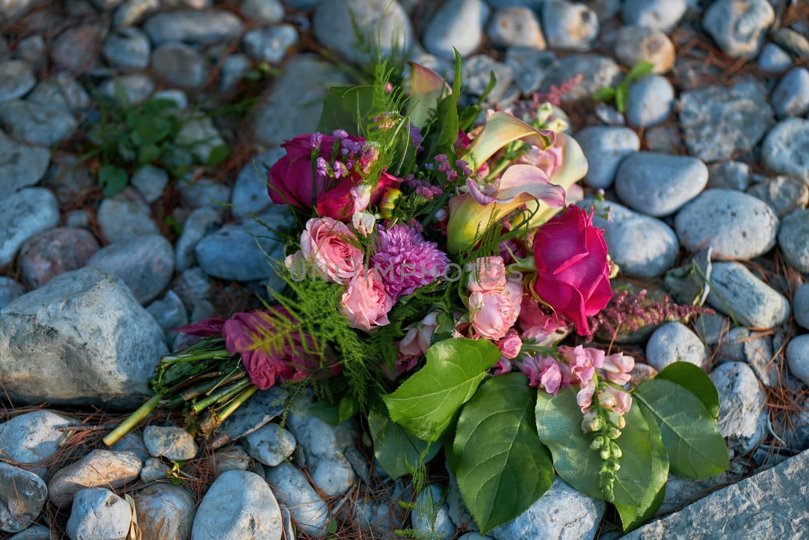 Wedding flowers, bridal bouquet closeup with roses and lilies on a Pebble and Rock Background with ambient evening lighting