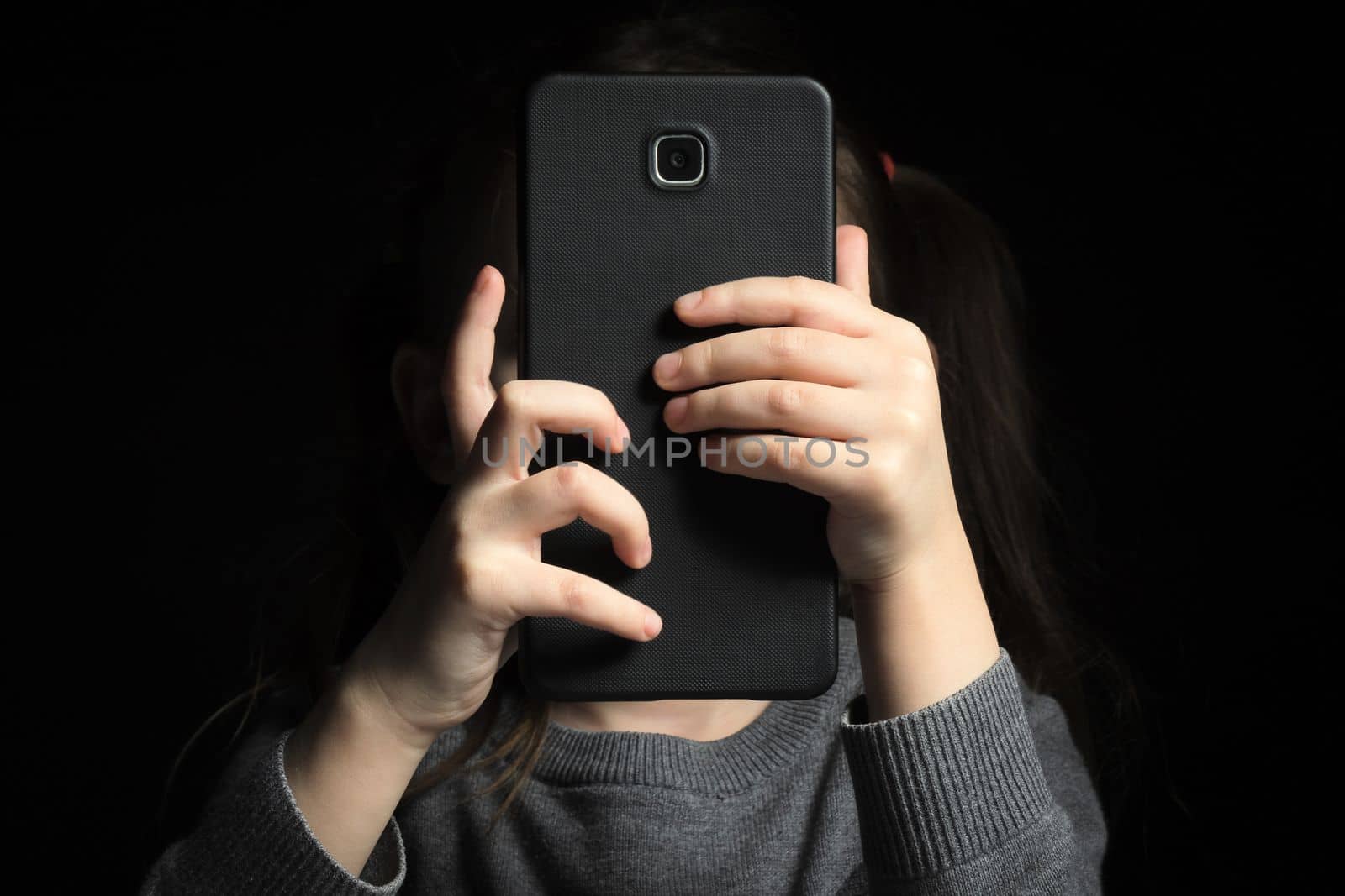 A large smartphone in children's hands, because of which the face is not visible. Kid gadget addiction and insomnia, psychological problems.