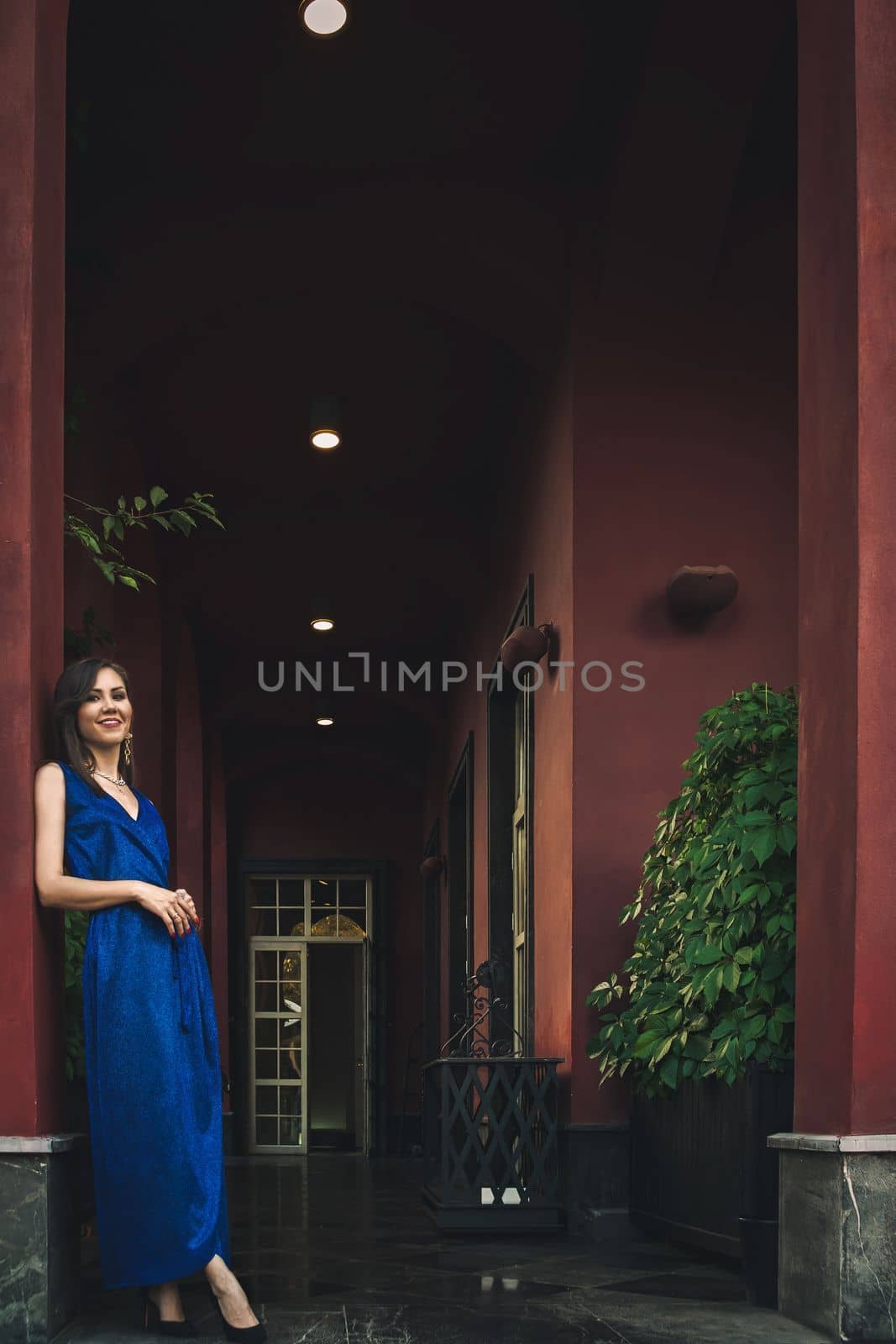 Young woman in blue dress next to exterior of big luxury house.