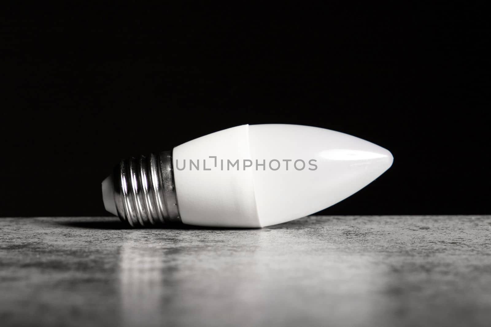 LED energy-saving lamp with E27 screw cap base in form of candle, on black background, copy space.