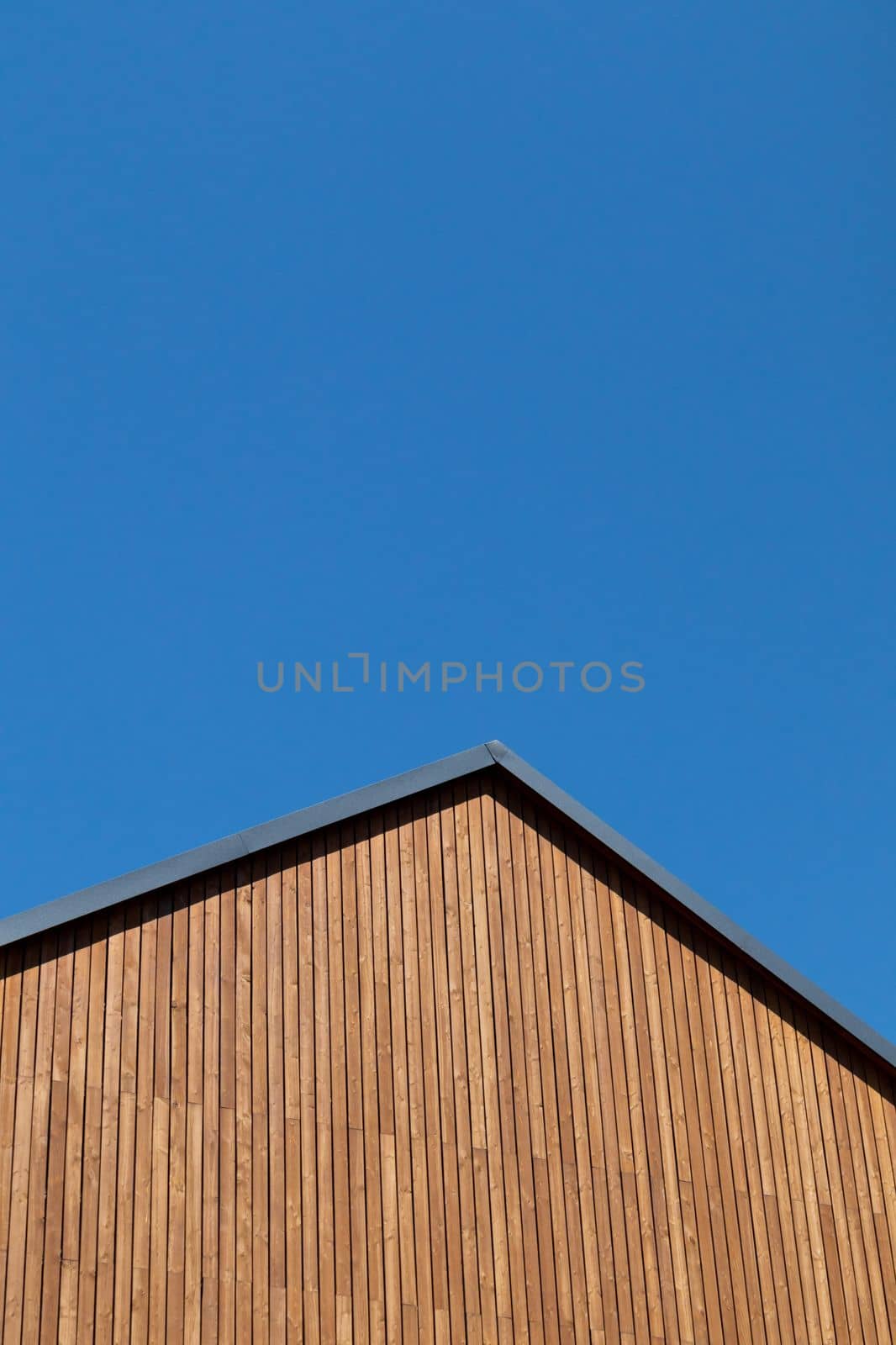 Rooftop with wooden plank gable on new modern home against clear blue sky.