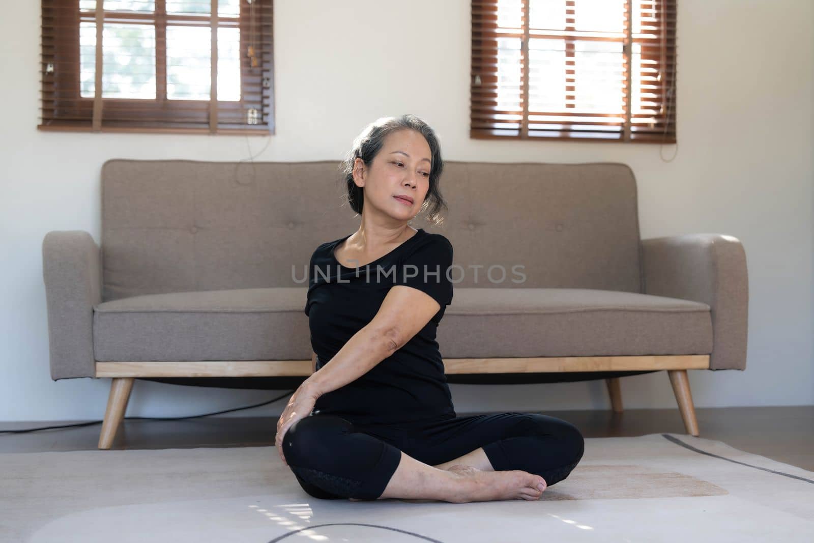 Healthy and happy 60s retired Asian woman in workout clothes practicing yoga in her living room...