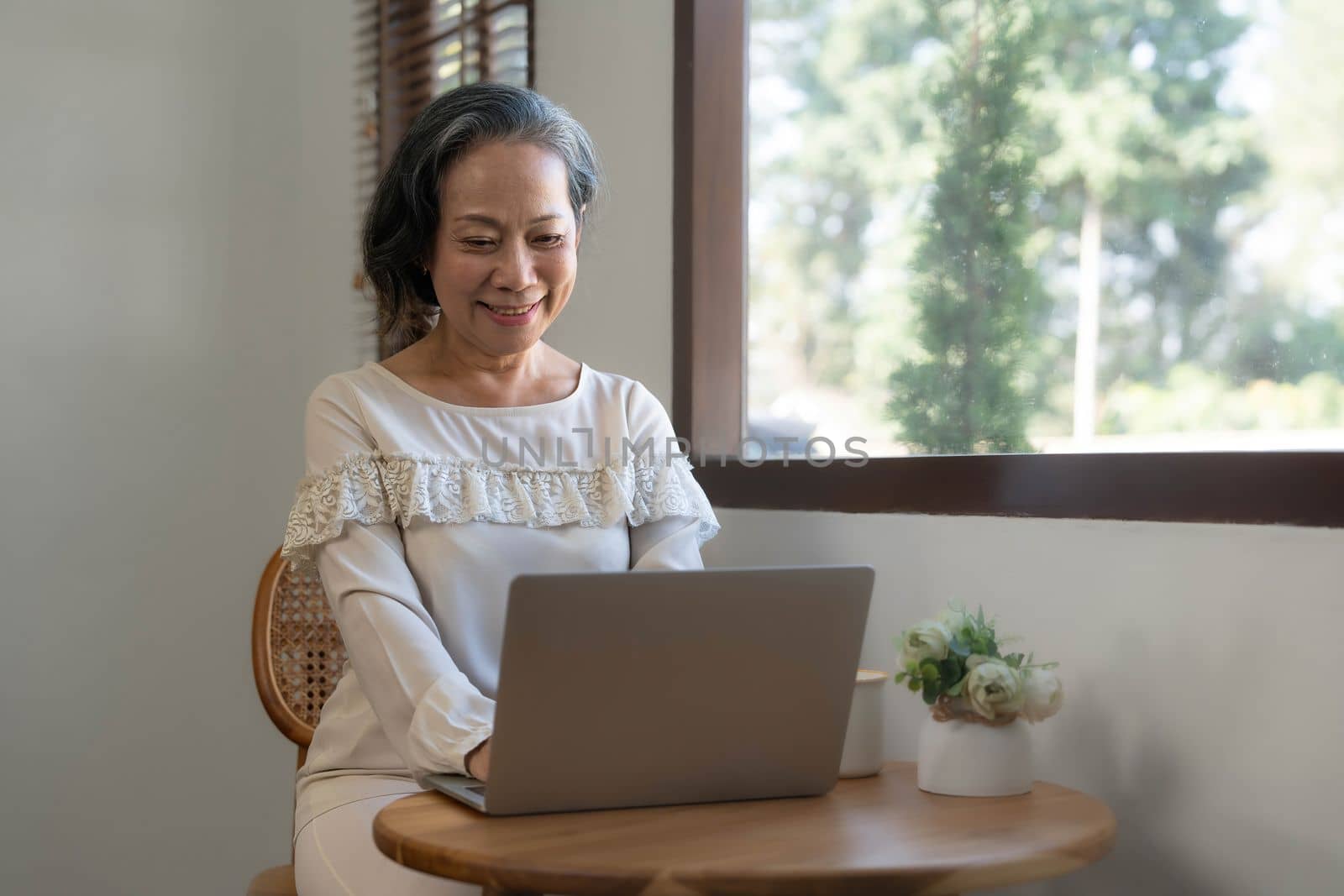 Portrait, Professional and successful aged Asian businesswoman working from home, sipping morning coffee while using laptop computer...